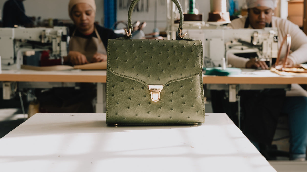 A Tuska ostrich leather bag on the workbench of the Cape Town atelier, artisans at their sewing machines behind